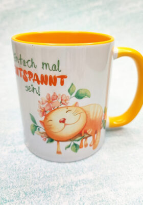 die Katzen mögen. Sie ist in einem fröhlichen Gelb gehalten und mit einem Spruch "Einfach mal entspannt sein!" und einer gezeichneten schlafenden Katze verziert. Die Tasse von Super-Mug ist sowohl für Kinder als auch für Erwachsene geeignet und kann als Kaffeebecher